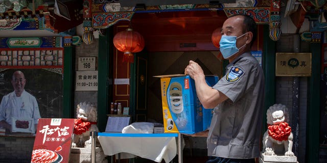 A security guard carries supplies past a reopened restaurant in Beijing Tuesday, May 12, 2020. 