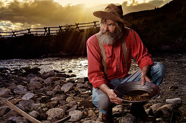 old-prospector-panning-for-gold-in-a-western-sunset-picture-id181137155